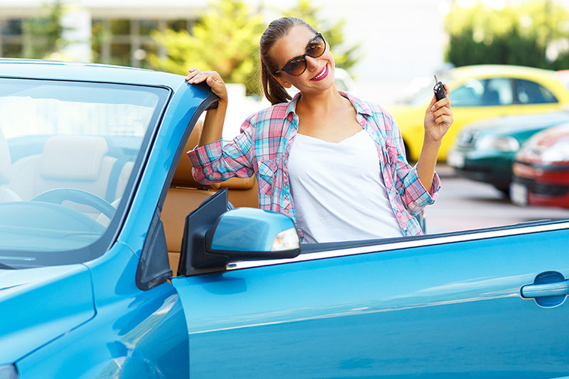 Giovane donna felice accanto alla sua nuova auto con le chiavi in mano