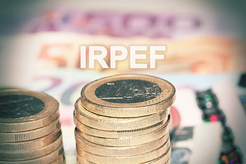 Pile di monete da 1 euro e scritta IRPEF in bianco su fondo sfocato.